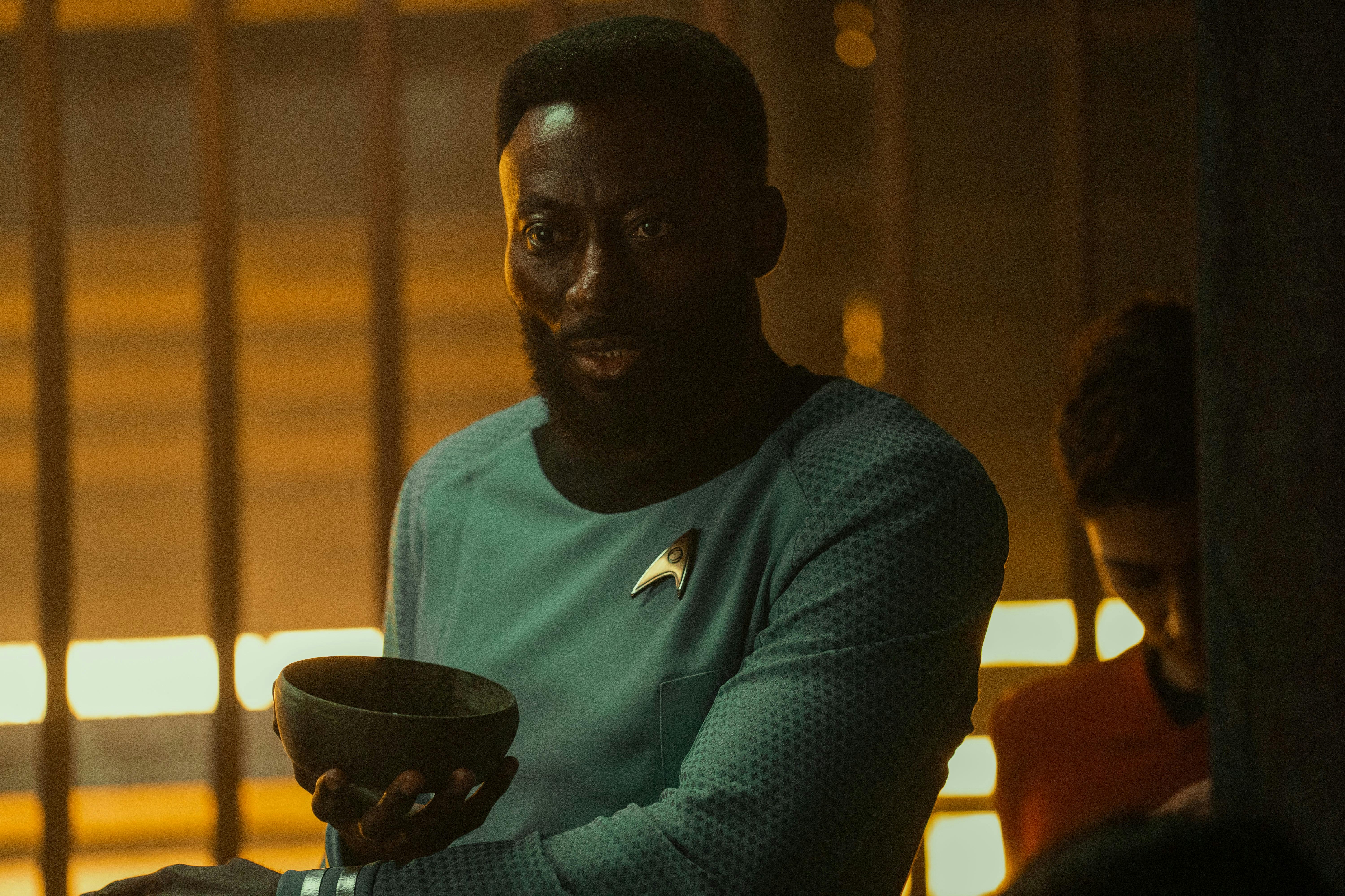 Dr. M'Benga (Babs Olusanmokun) holds a tricorder and looks concerned.