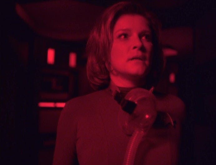 Captain Janeway looks fearful in a hallway full of red light.