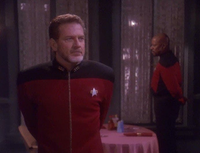 Leyton stands stern with his arms behind his back Sisko doing the same a few feet away looking straight in another direction on Deep Space Nine's Paradise Lost