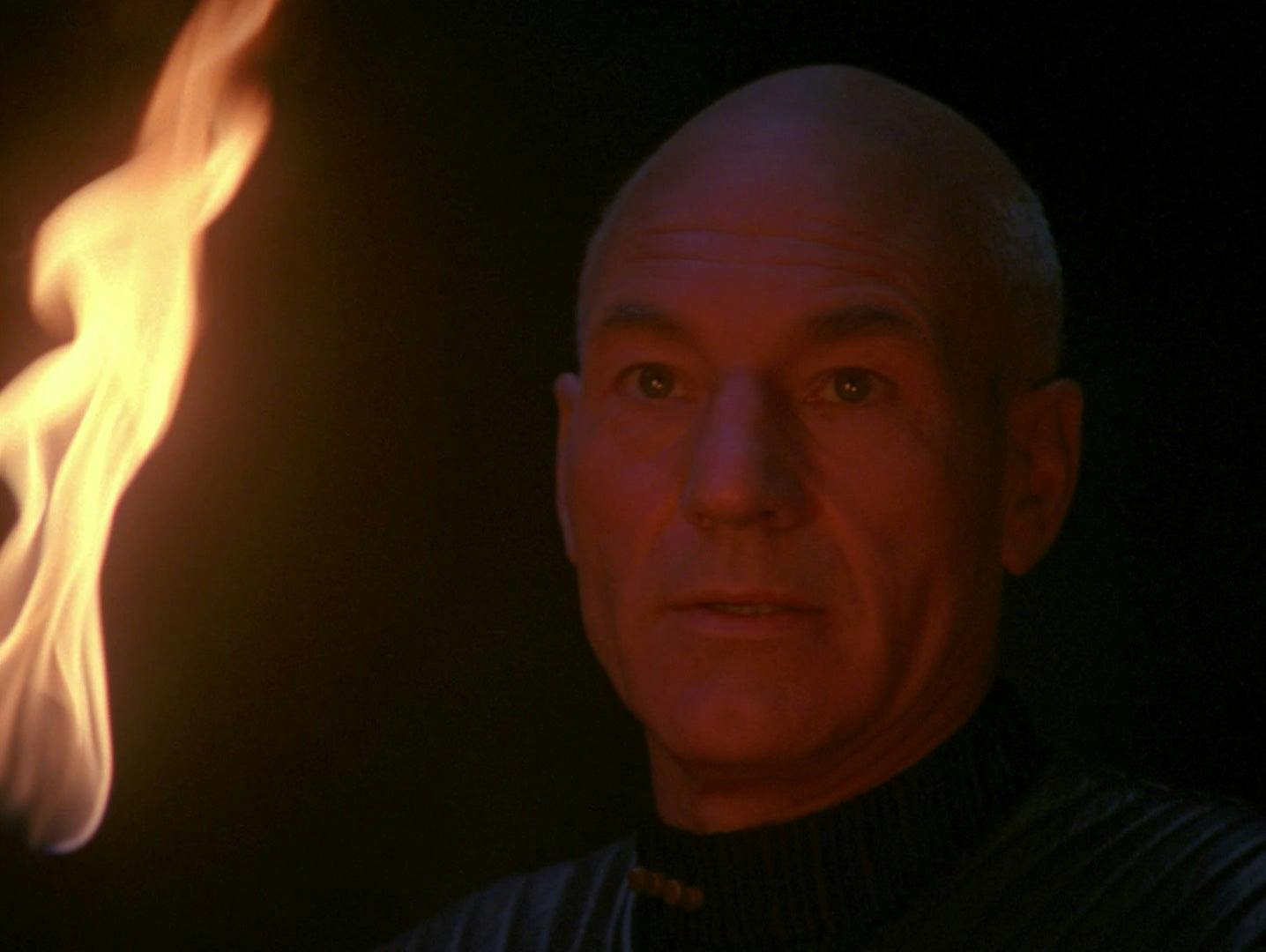 Close-up of Picard holding a lit torch near his face on the surface of a planet at night in 'Darmok'