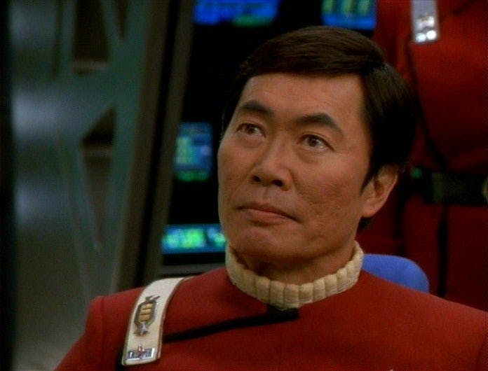 Captain Hikaru Sulu (The Original Series) sits in the captain's chair, wearing the red uniforms of the original Star Trek movies. This is a flashback from the Voyager episode 