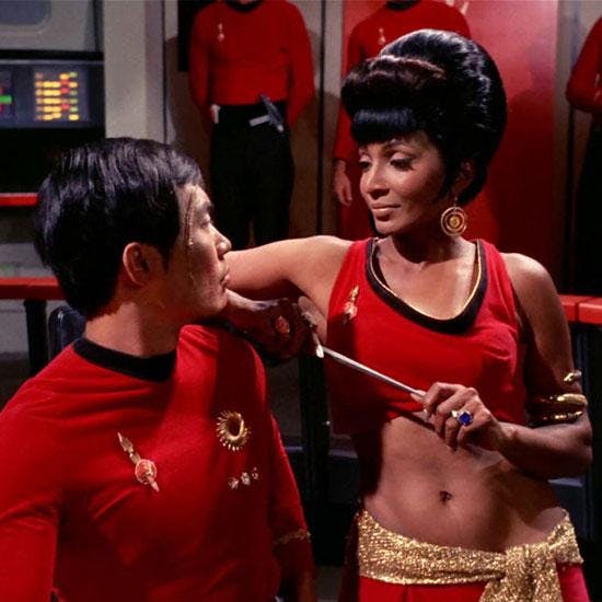 Mirror Uhura holding a dagger with her elbow resting on a seated Sulu