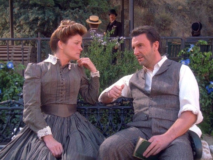 In 'Fair Haven,' donning period-appropriate civilian attire, Captain Janeway sits on a bench besides holo-bartender Michael Sullivan