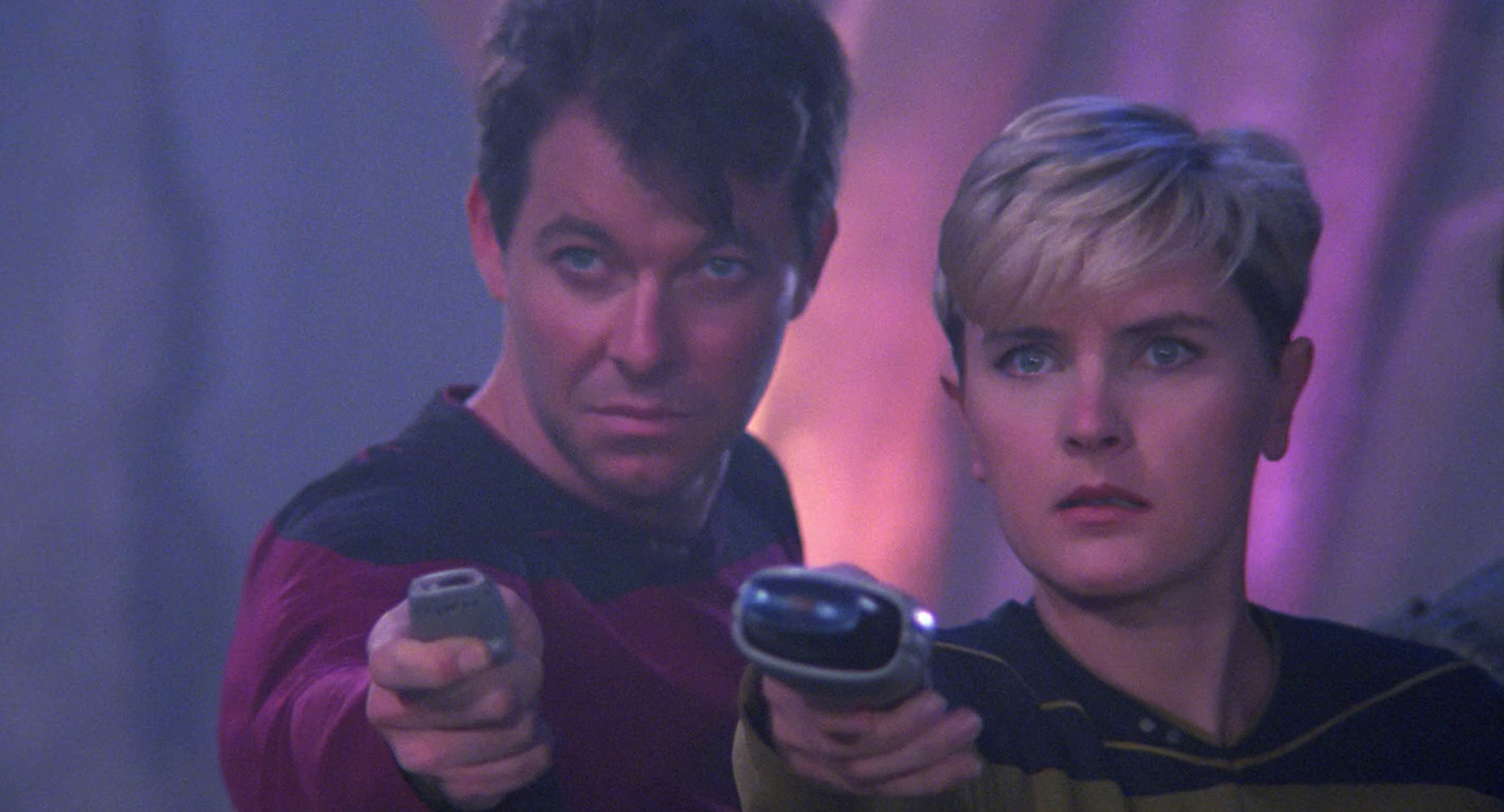 Still of Will Riker and Tasha Yar holding up their phasers in a defensive stance