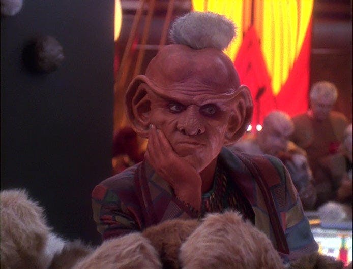 Quark looks unhappy as a tribble rests on his head.