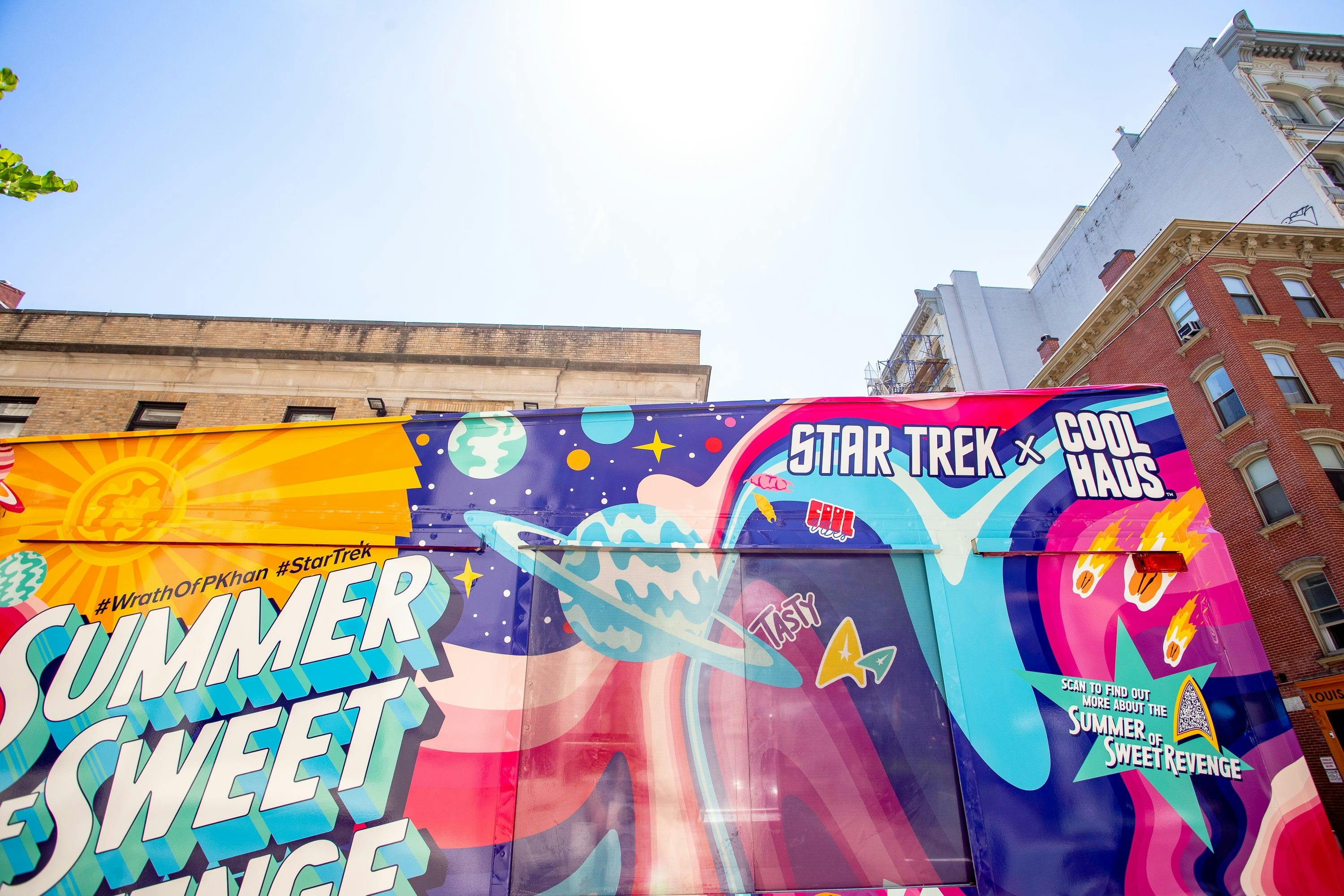 Blue skies and sunshine are visible over the top of the brightly colored ice cream truck.