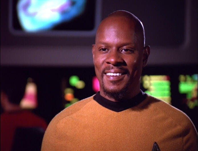 Captain Sisko (Avery Brooks) smiles as he wears the gold TOS uniform.