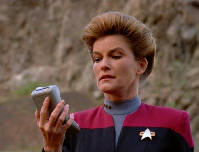 Captain Janeway lifts a tricorder and reads from it in 'The 37s'