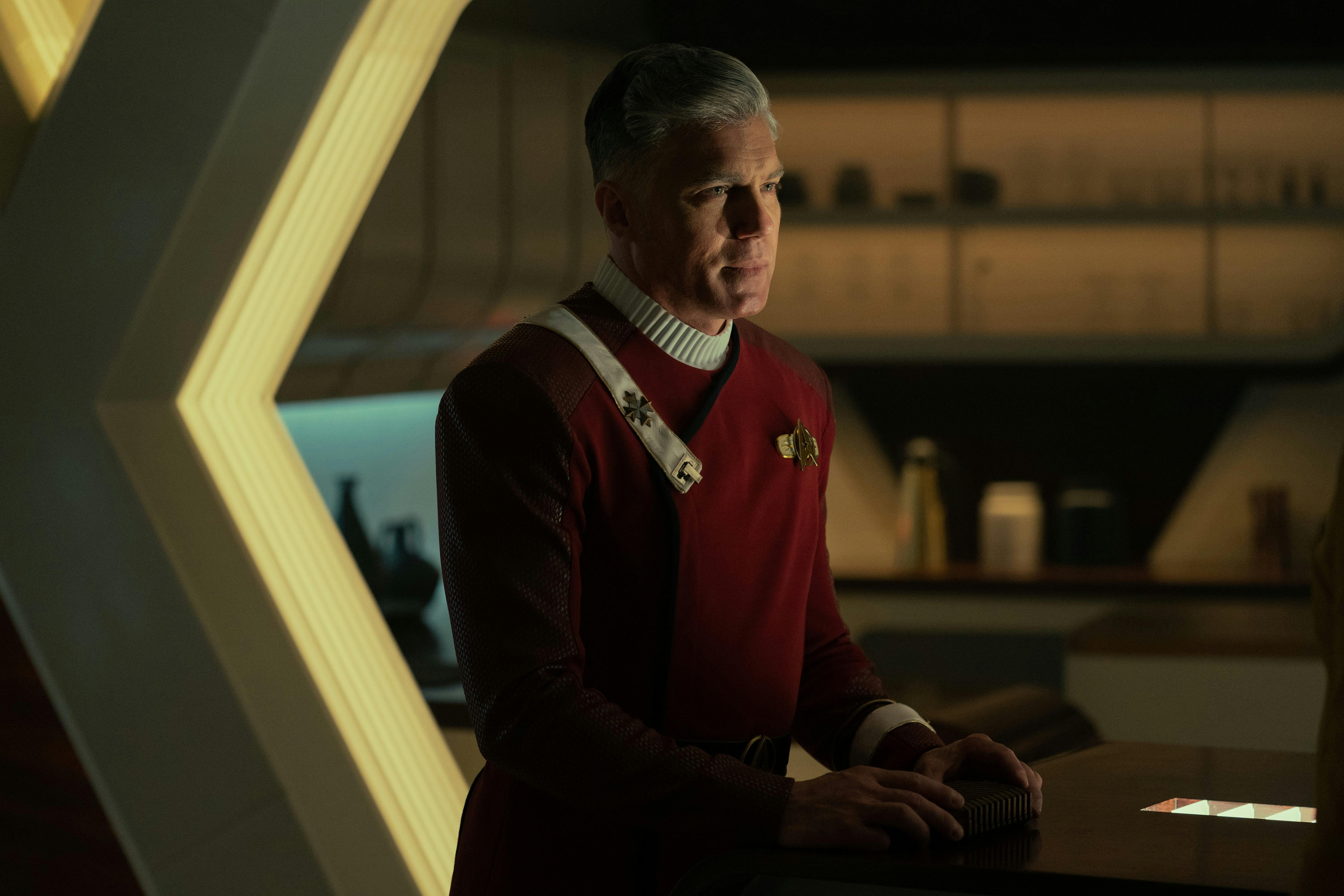 Captain Pike (Anson Mount) stands in his quarters, wearing the red uniform from Star Trek II: The Wrath of Khan.