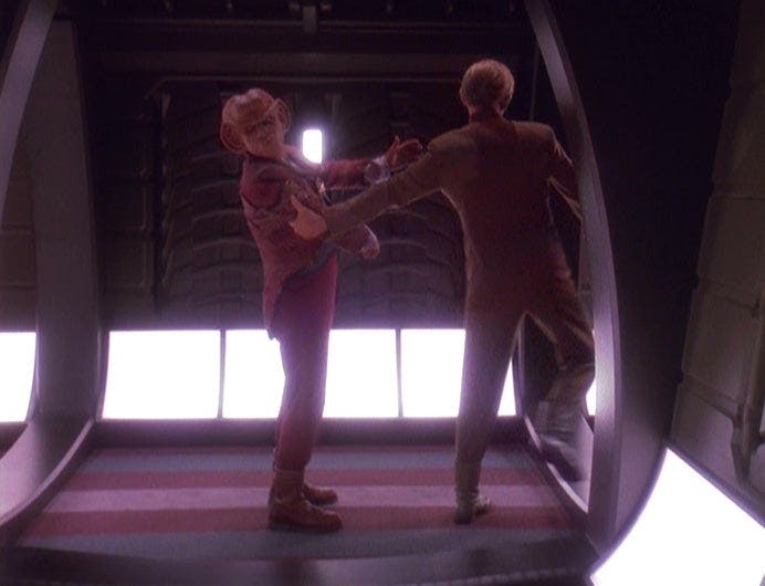 In a corridor, Odo with his back to us grabs Quark by his arm to pull him away on Star Trek: Deep Space Nine