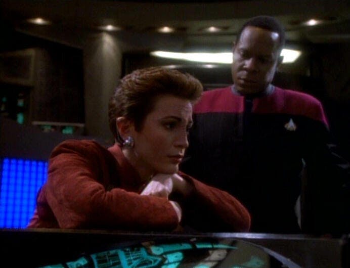 Major Kira glumly rests her head on her arms at her station as Commander Ben Sisko looks over in 'In the Hands of the Prophets'
