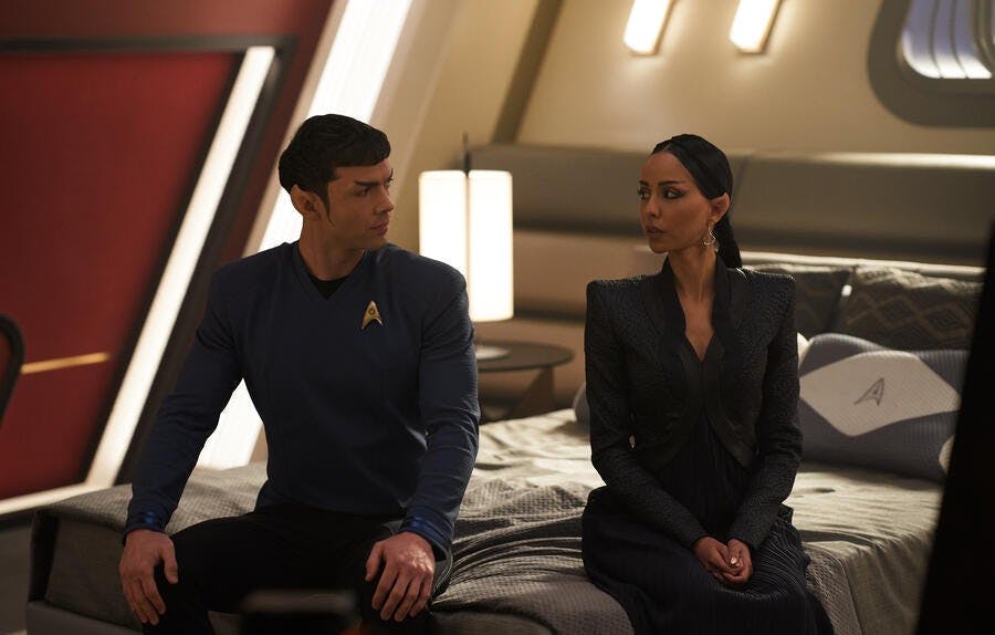 Spock and T'Pring (Strange New Worlds) sit on a bed while looking at each other.