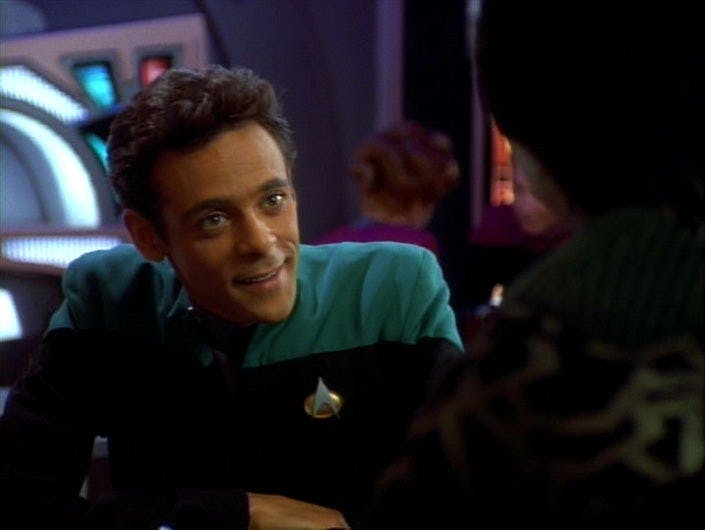 Bashir sits across from Garak and smiles on Star Trek: Deep Space Nine