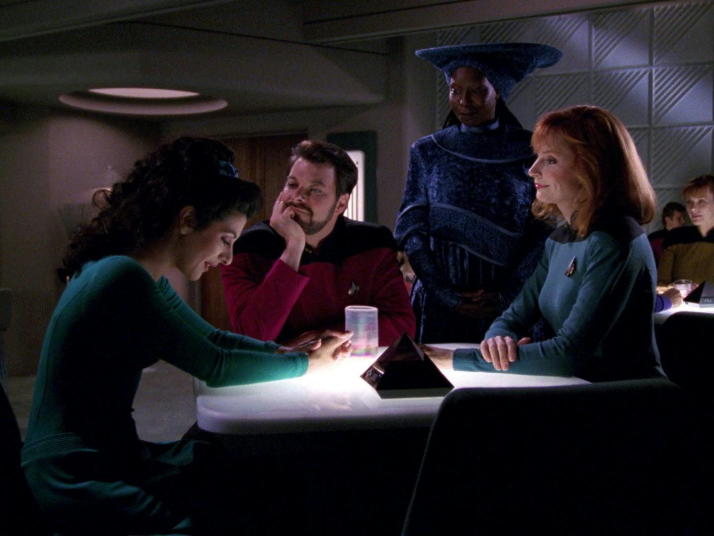Deanna Troi sits at 10 Forward surrounding by the love and support of friends Riker, Guinan, and Dr. Beverly Crusher