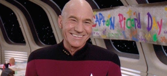 Picard smiles in front of the Captain Picard Day banner on Star Trek: The Next Generation