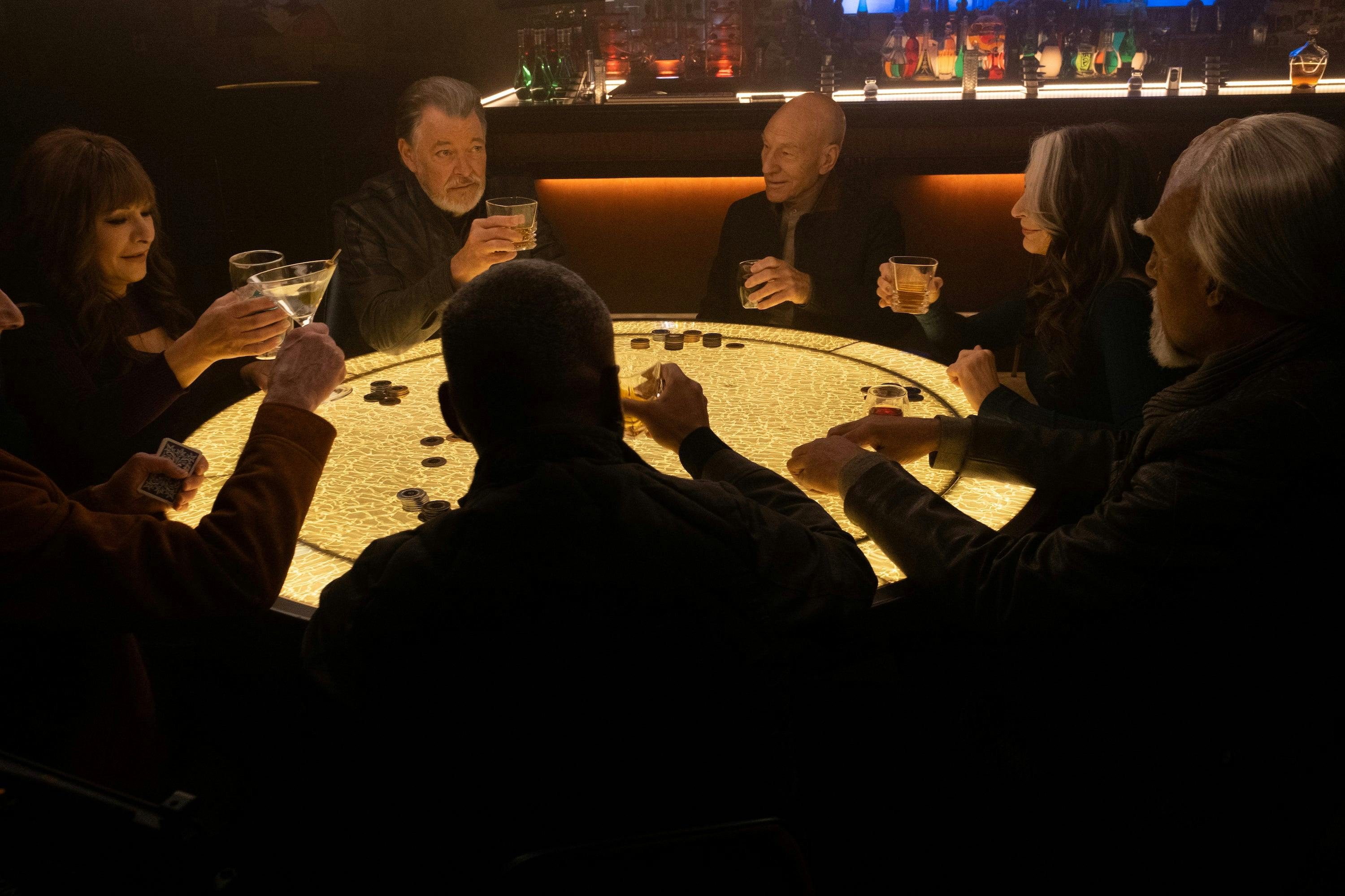 The original Enterprise-D crew (Deanna, Riker, Picard, Beverly, Worf, Geordi, and Data) sit around the poker table while raising a glass in 'The Last Generation'