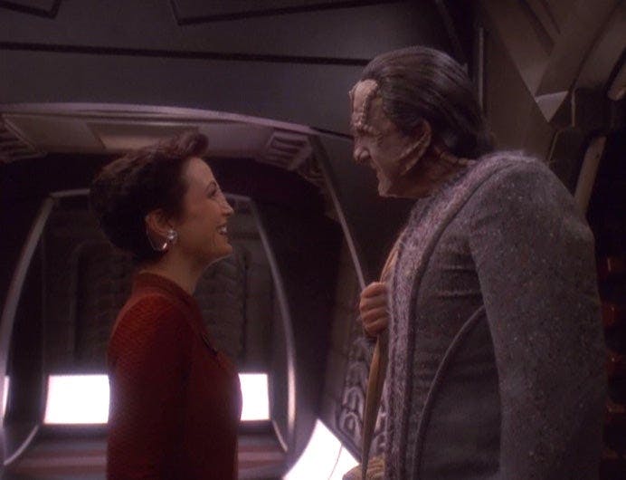 In a corridor, Kira brightly smiles at the Cardassian Tekeny Ghemor in 'Ties of Blood and Water'