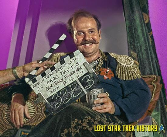 Behind-the-scenes promotional photo of Roger C. Carmel as Harry Mudd sitting on-set with a clapboard in front of him with details from the Desilu 'Star Trek' production of 'I, Mudd'