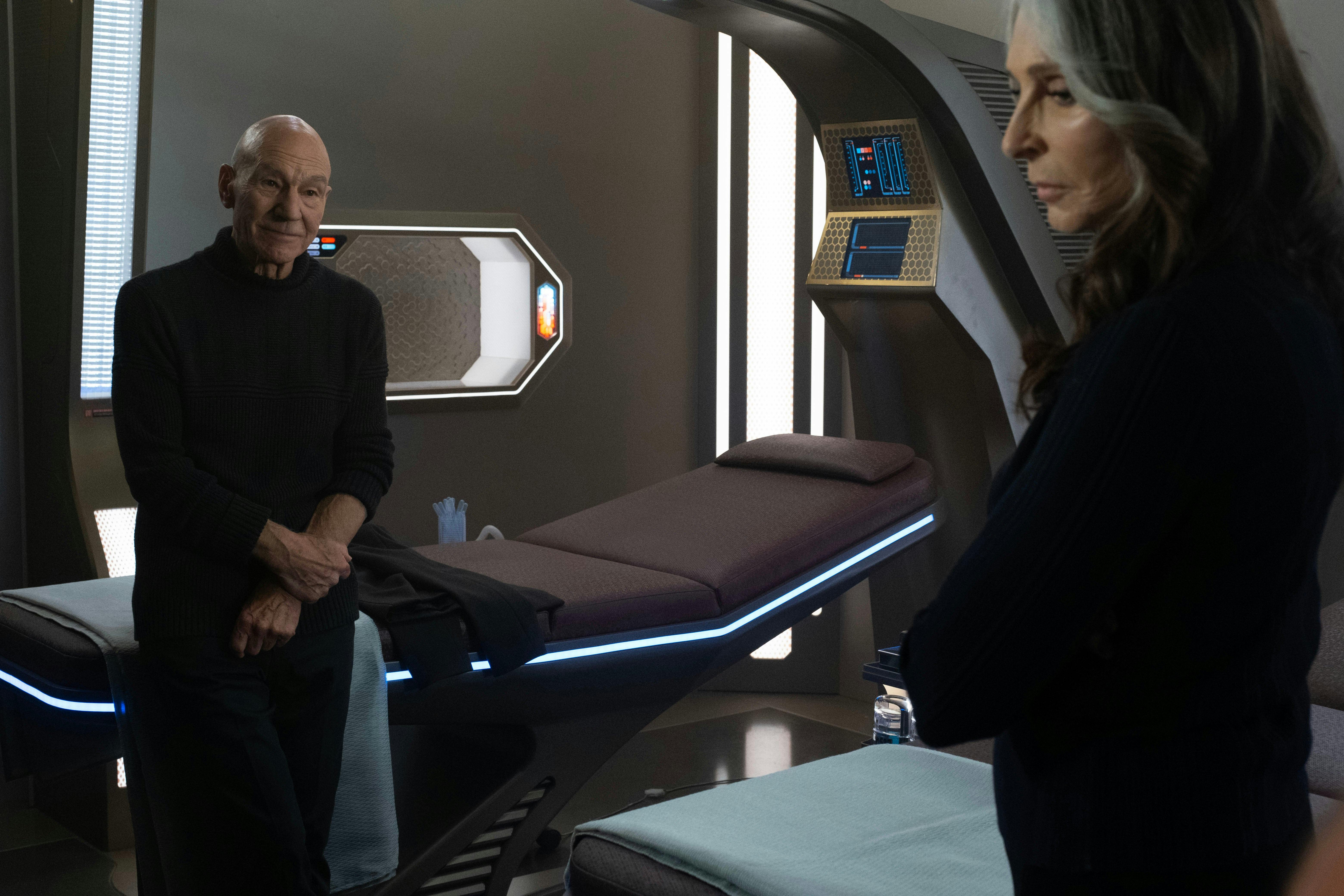 Picard sits on a med bed to talk to Beverly as she looks away on Star Trek: Picard