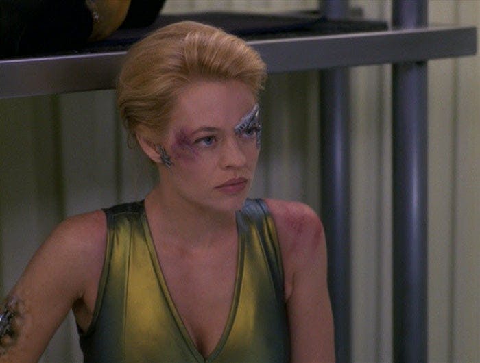 Seven of Nine, wearing a tank top, looks at someone. She has bruises on her face.