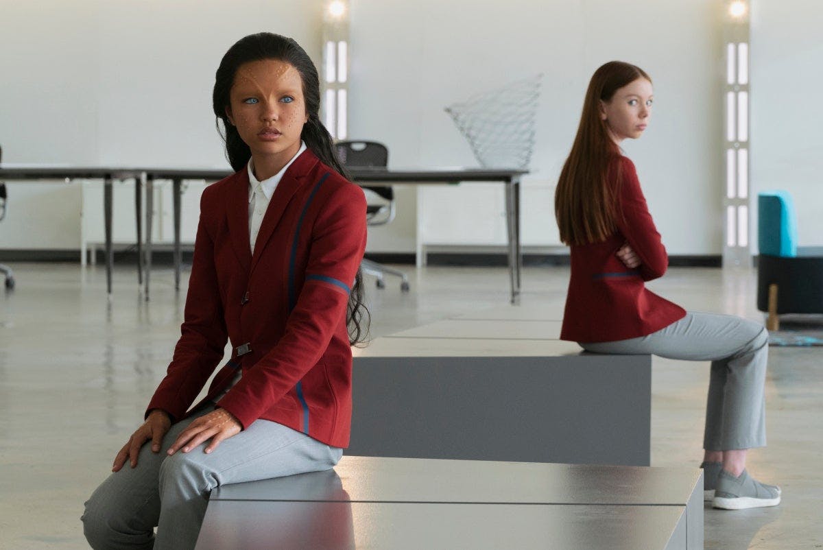 Kima and Lil in their school uniforms sit diagonal with their backs toward each other at school in 'Children of Mars'