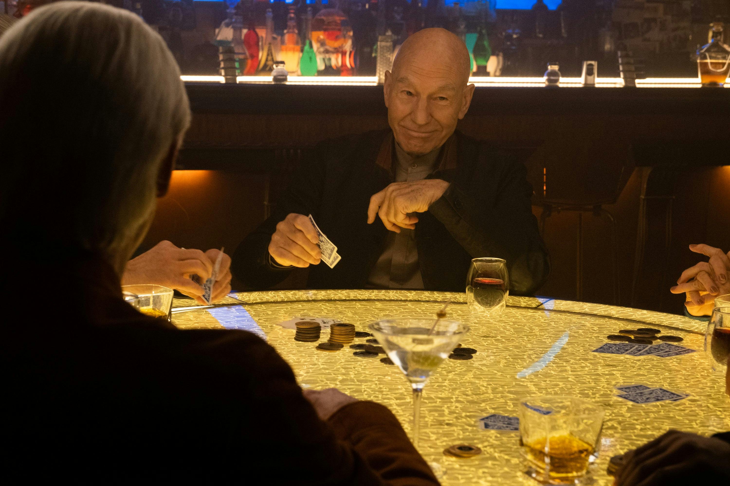 Jean-Luc Picard smiles at his crew while holding his poker cards and looking ahead in 'The Last Generation'