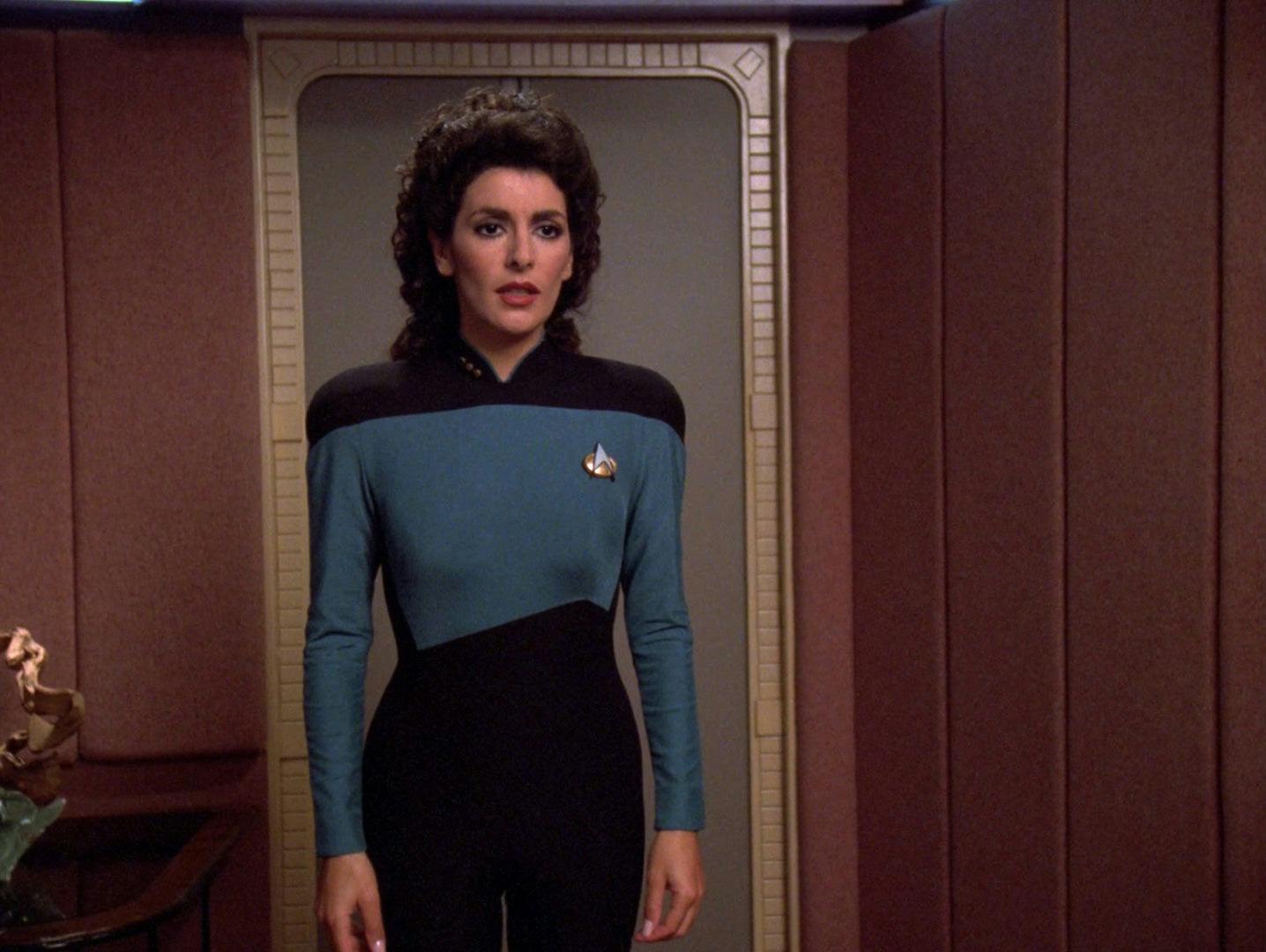 Deanna Troi, wearing her Starfleet uniform, addresses Jellico in his ready room