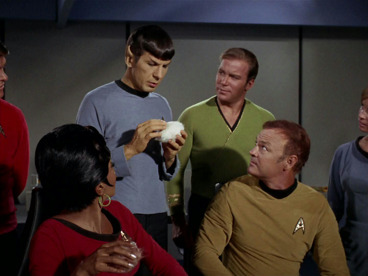 Spock cuddles a tribble as Kirk, Uhura, and another crewmember look on.