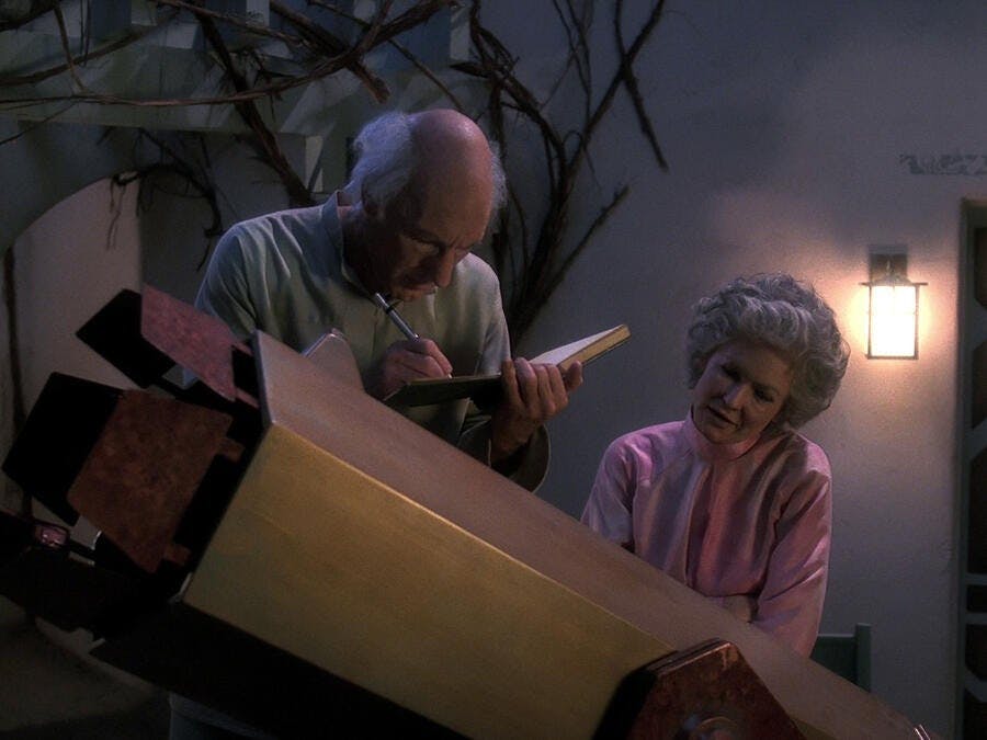 Picard as Kamin uses his telescope to study their planet's conditions and jots down his notes as his wife Eline stands beside him in 'Inner Light'