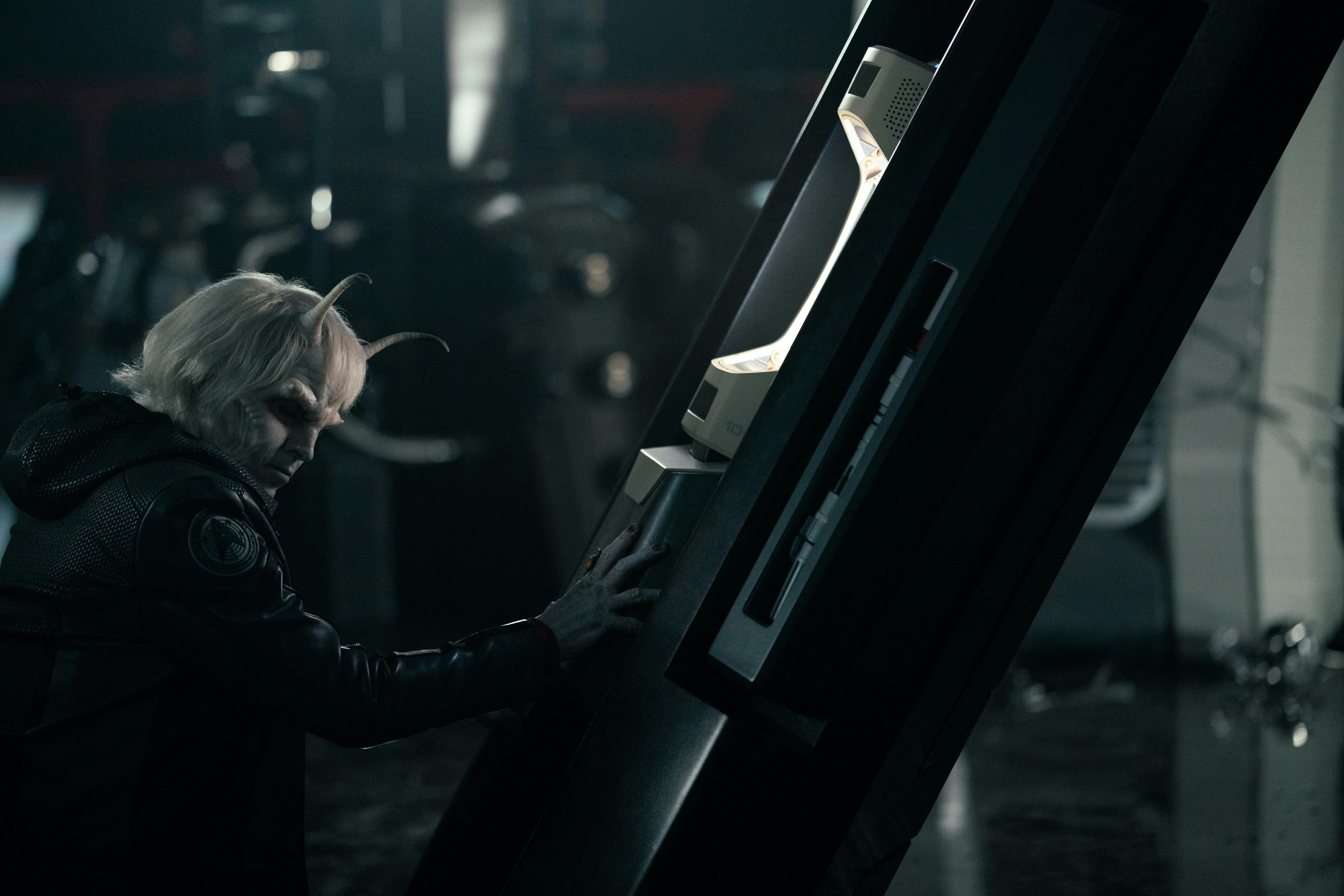 Hemmer (Bruce Horak) stands near a console in a dark room.