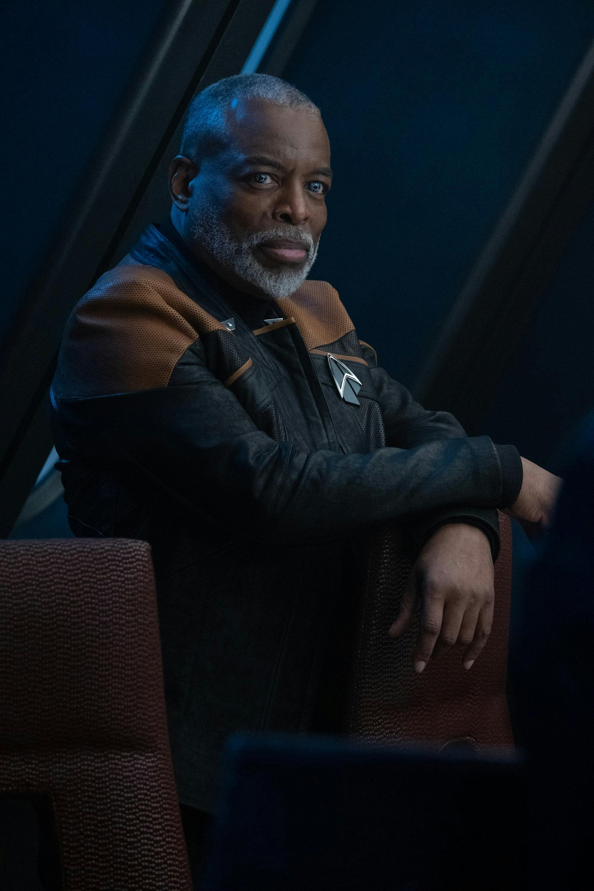 Geordi La Forge sits at the table in the Titan's Observation Lounge with his right arm crossed over his left