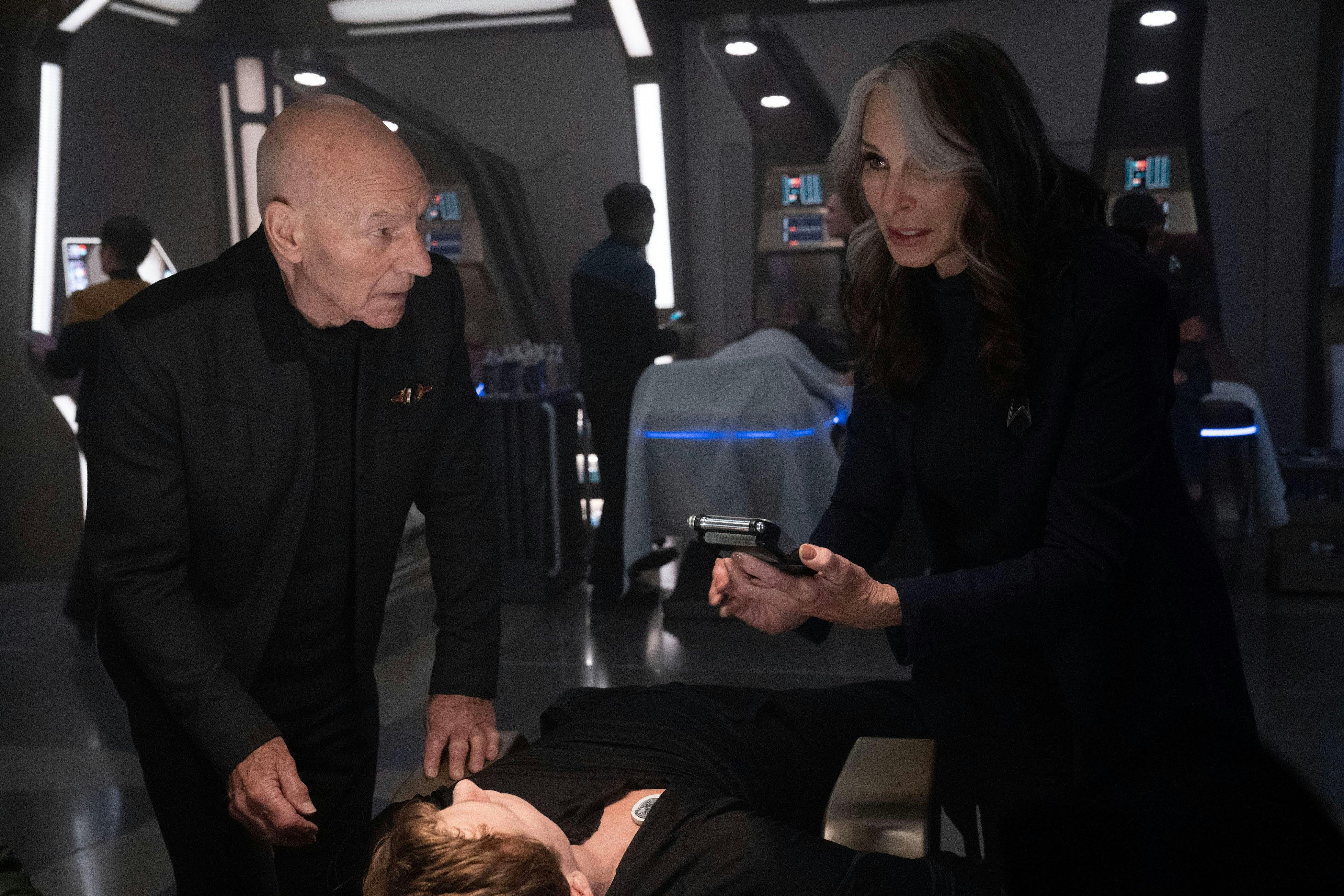 In Sickbay, Dr. Beverly Crusher looks over a poisoned Jack Crusher's vitals as a concerned Picard stands by
