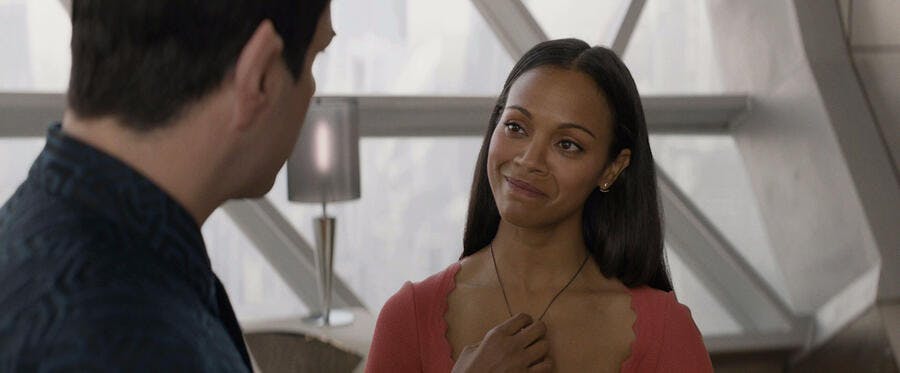 Uhura warmly looks over at Spock while touching her necklace pendant in Star Trek Beyond