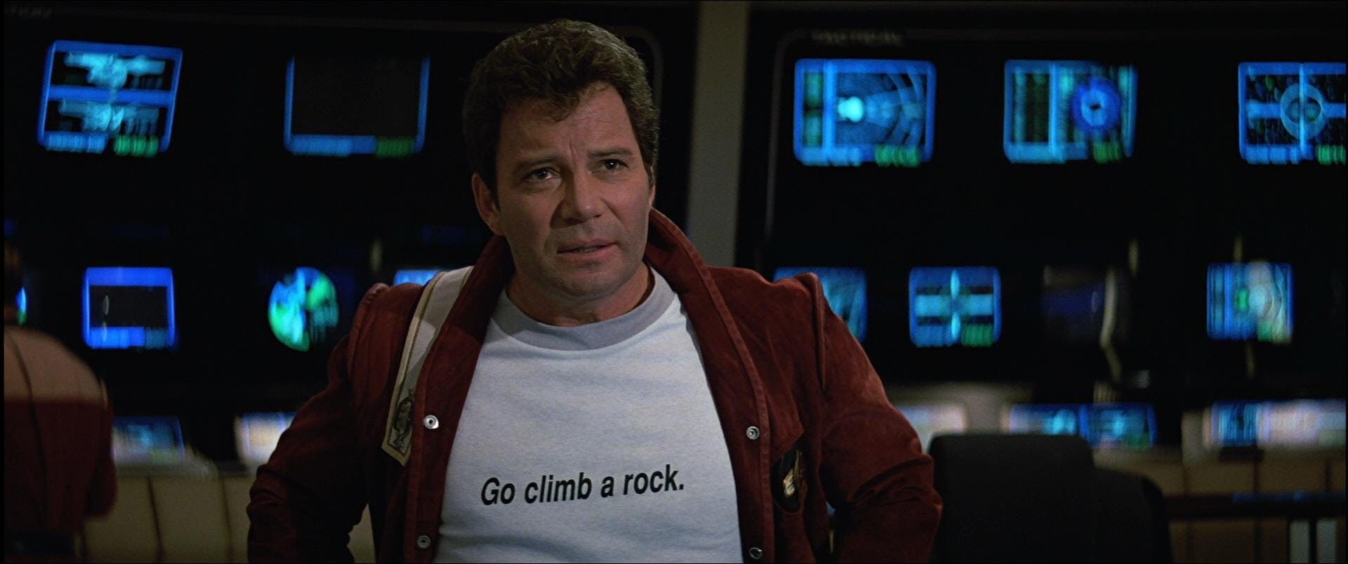 Close-up of Jim Kirk on the bridge in a 'Go climb a rock' shirt in Star Trek V: The Final Frontier