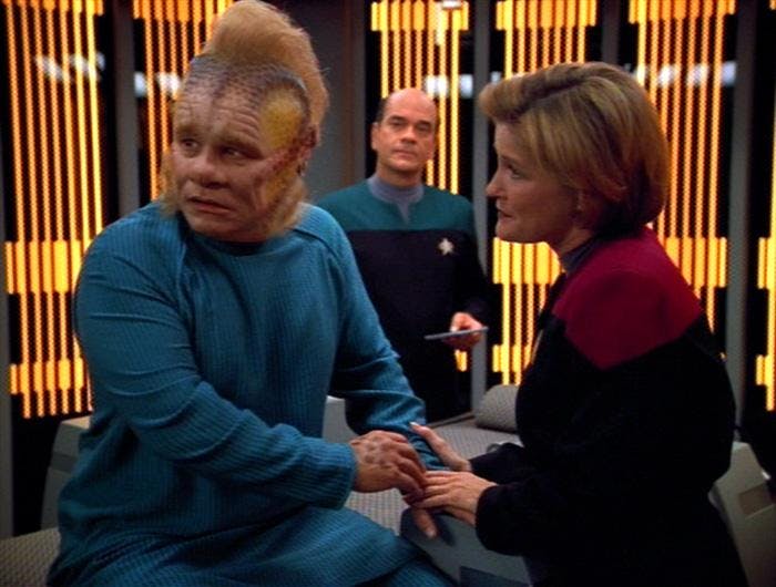 Janeway holds Neelix's hand as he looks over his shoulder while The Doctor looks on Star Trek: Voyager