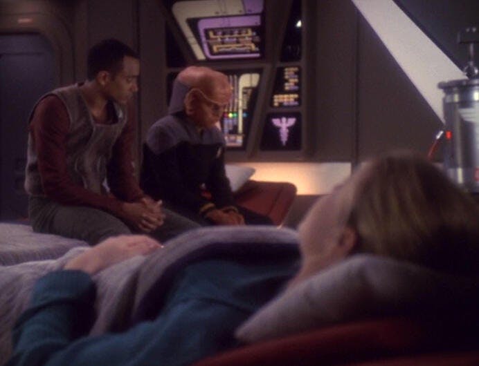 In a hospital bed, Dorian Collins looks over at the solemn Jake Sisko and Nog in Sickbay in 'Valiant'