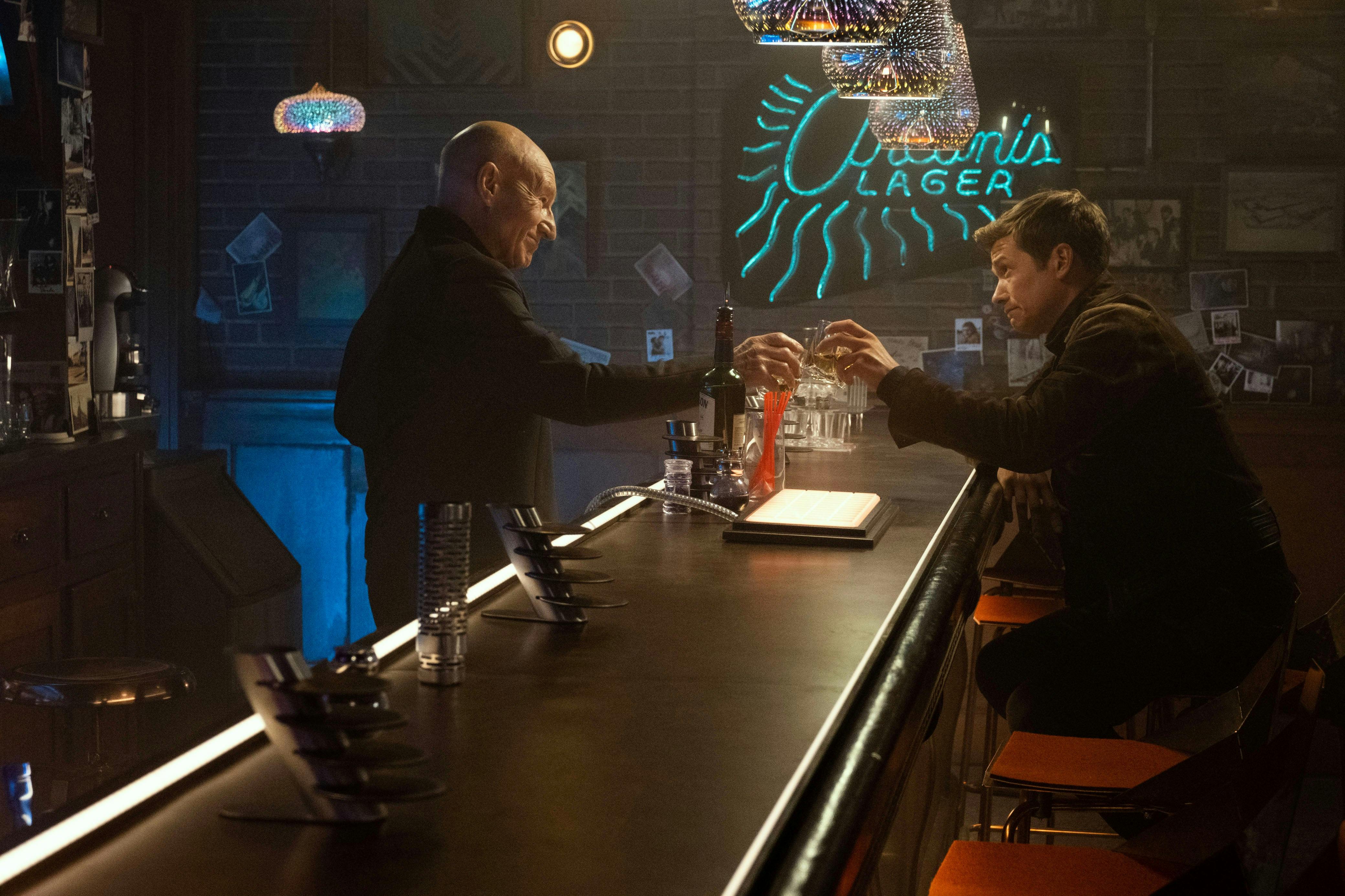 At the 10 Forward holoprogram, Picard pours a drink for himself and Jack Crusher as they raise their glasses together