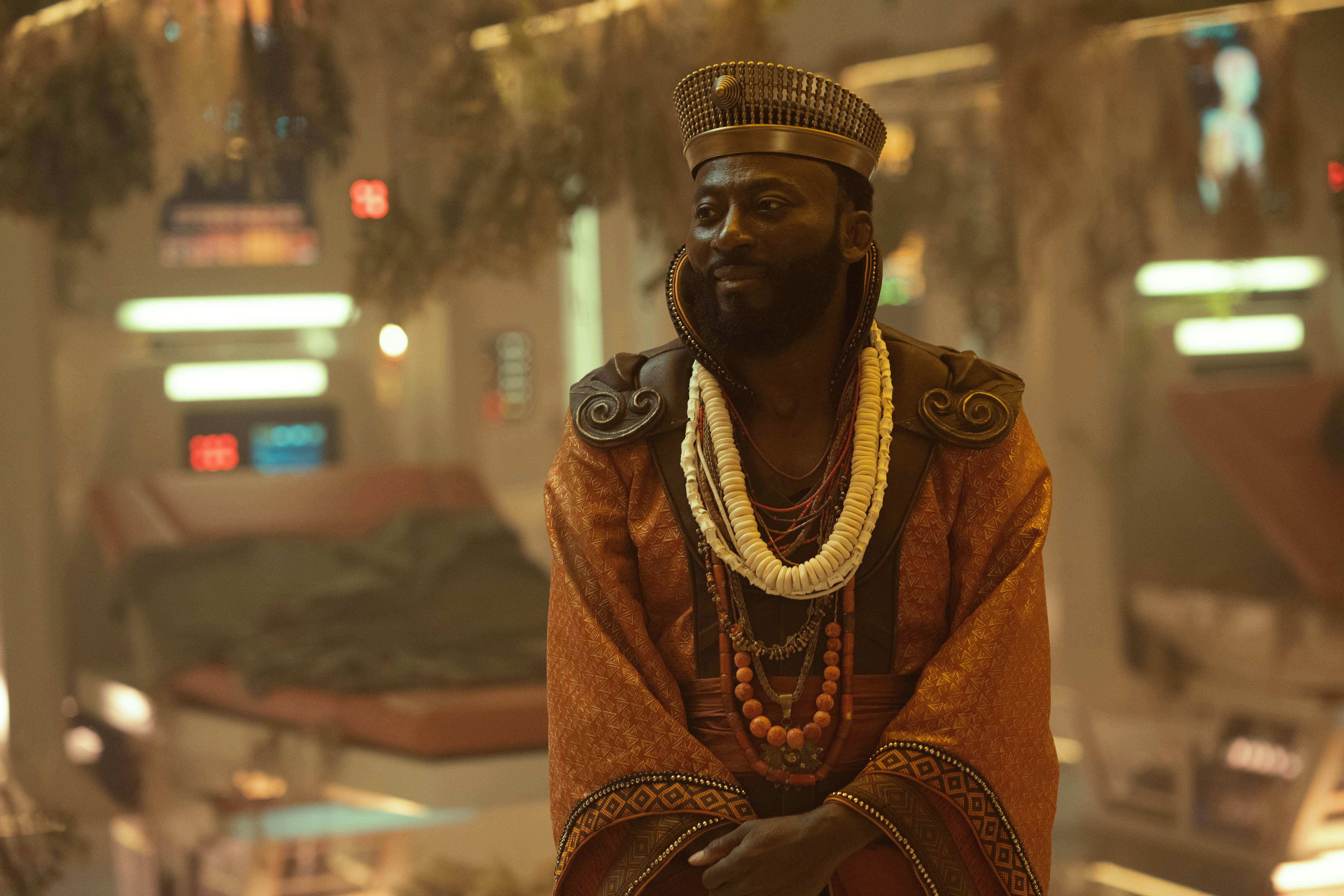 Dr. M'Benga (Babs Olusanmokun) stands in sickbay, wearing a crown and robe.