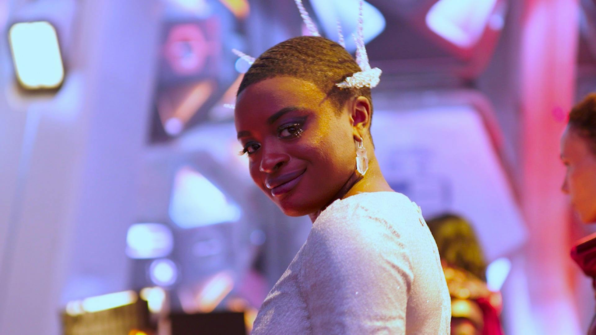 Celia Rose Gooding, who plays Cadet Uhura, smiles as she prepares for the role-within-a-role of Queen Neve. She is wearing an elaborate costume.