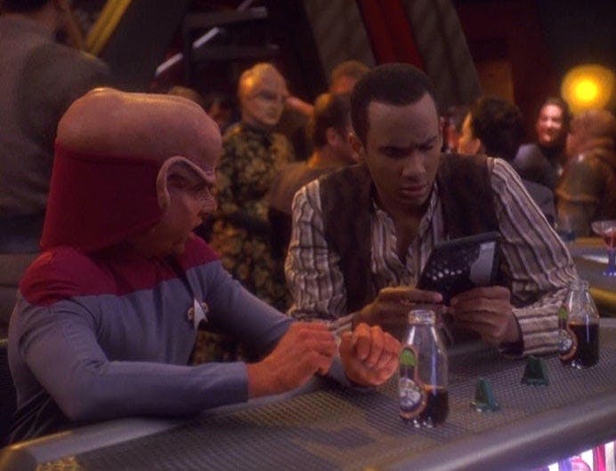 Nog and Jake Sisko sit at Quark's Bar looking at a Willie Mays baseball card on Star Trek: Deep Space Nine