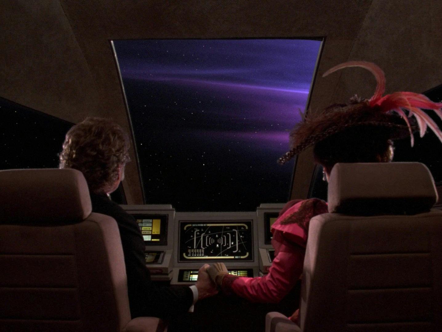 Professor Moriarty and his companion sit in a shuttle holding hands as they look out on the horizon ahead of them