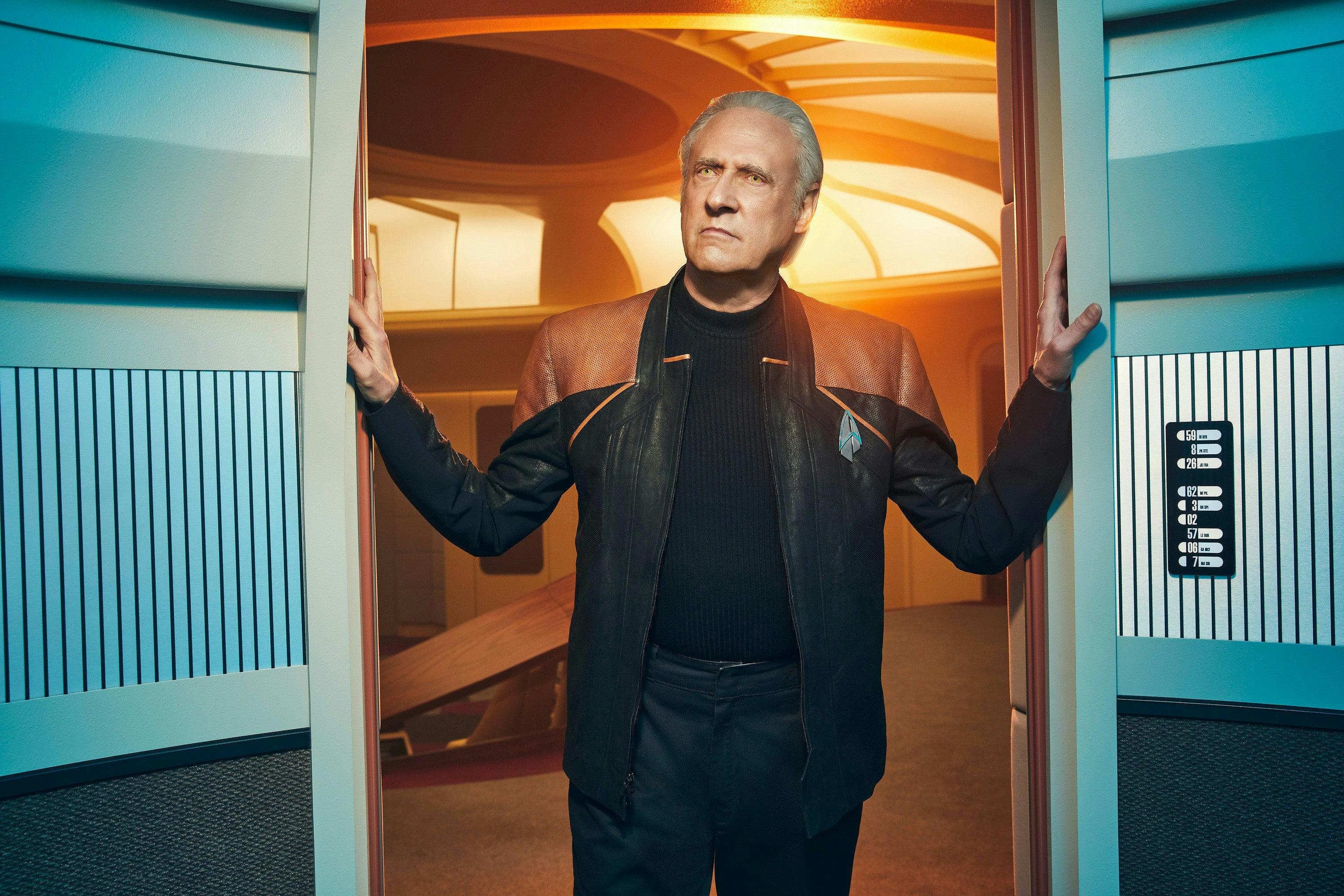 Promotional photo of Data at the entry of the turbolift with the Enterprise-D bridge behind him with both hands on the sides of the lift frame