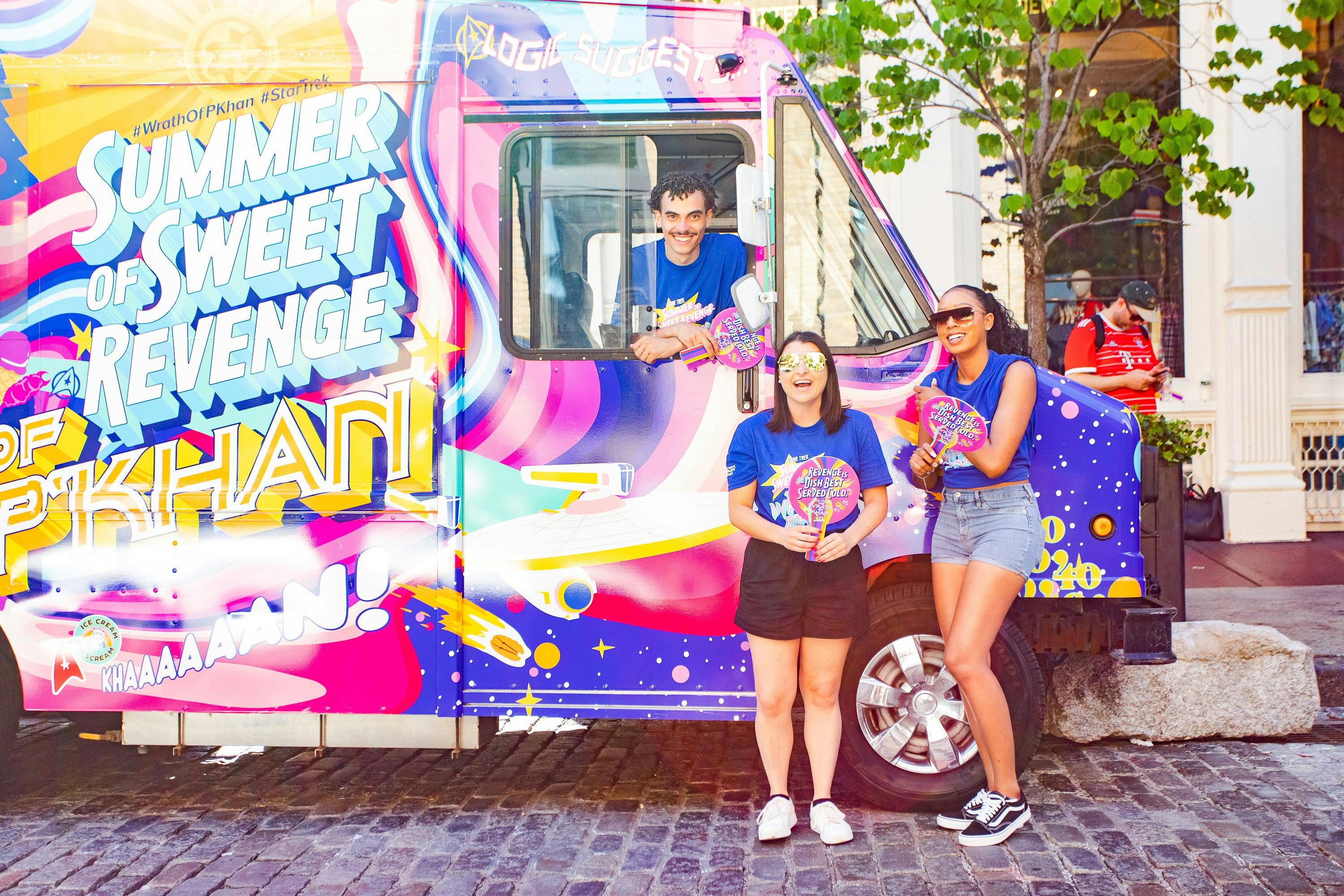 The three workers who served ice cream pose next to the truck. They are wearing blue shirts that have "The Summer of Sweet Revenge" and "The Wrath of P'Khan" on them, and are holding paper fans.