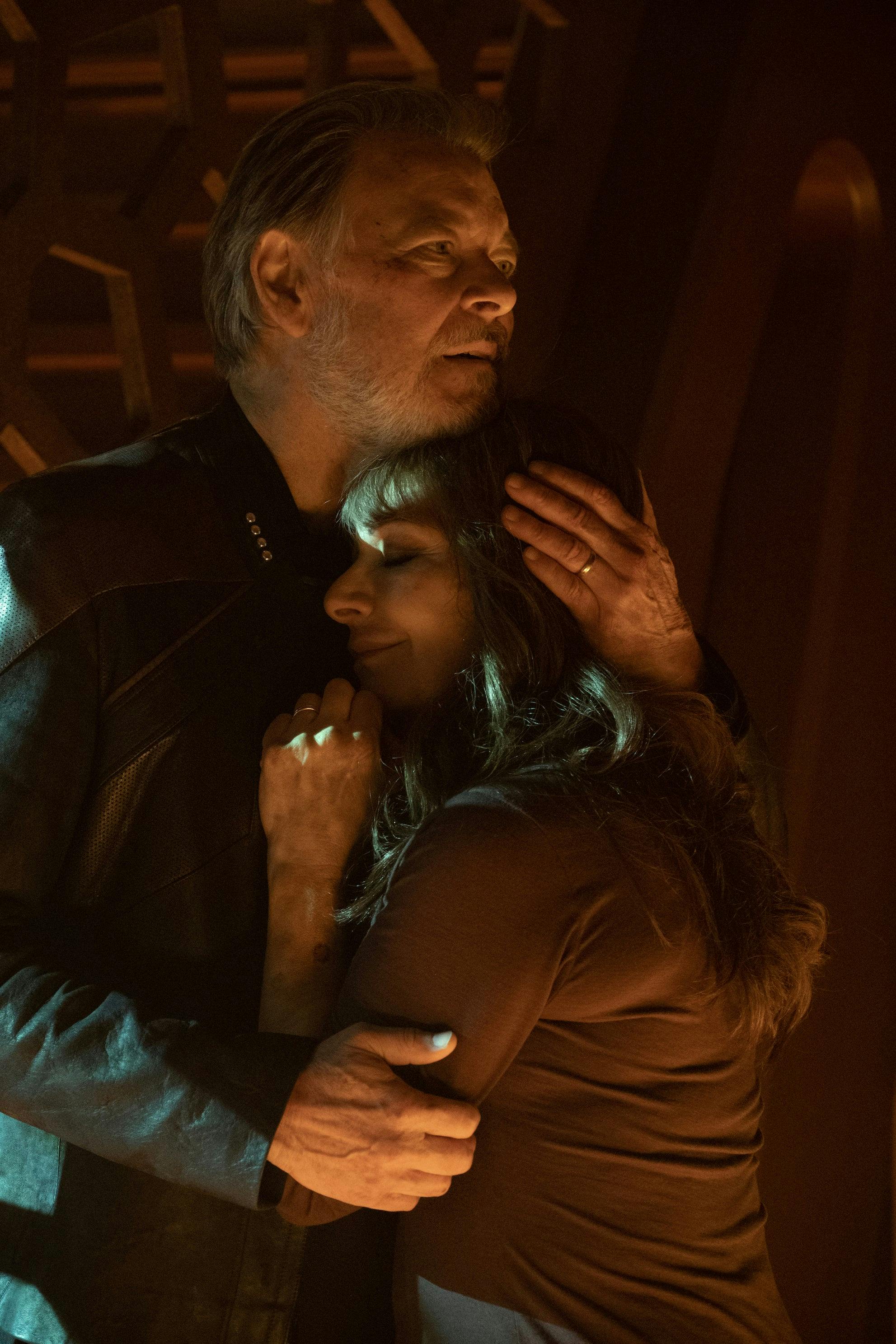 A battered Will Riker holds Deanna Troi in his arms, embracing her, as she smiles in comfort on the Shrike