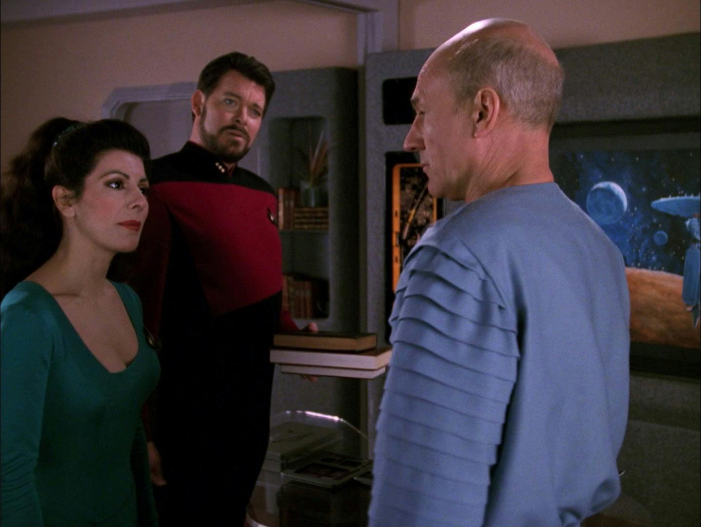 On the Enterprise, Deanna Troi and Will Riker standing next to each other both look at Captain Picard in his relaxed civilian wear in 'Captain's Holiday'