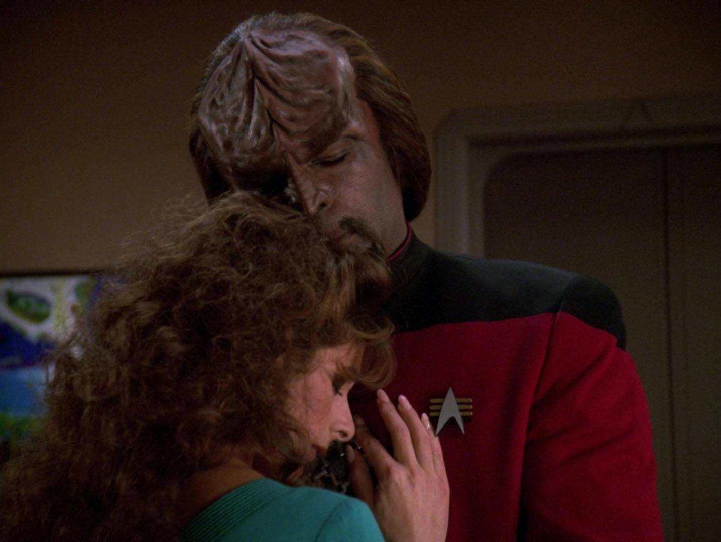 Worf holds Deanna Troi in a warm embrace as he rests gently on her head