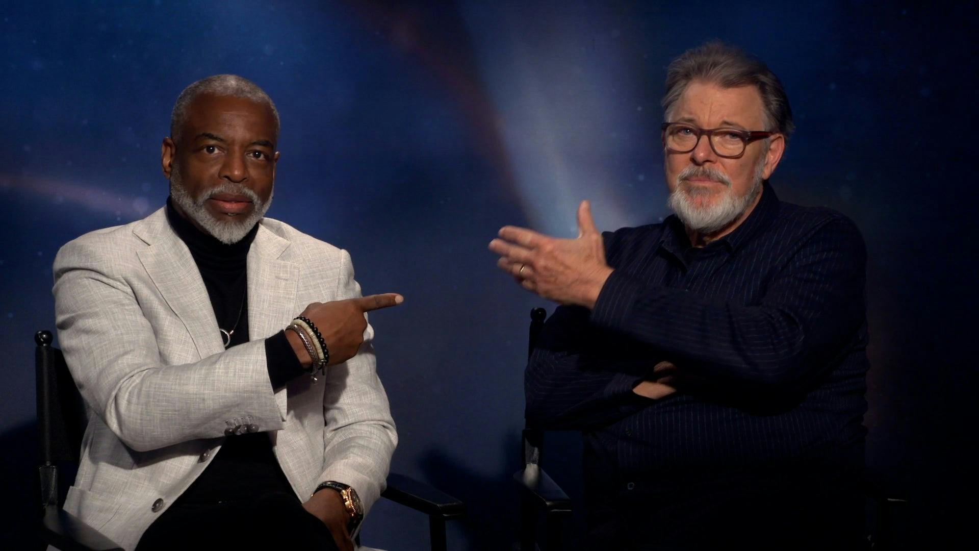 LeVar Burton points at Jonathan Frakes who holds his hand in LeVar's direction