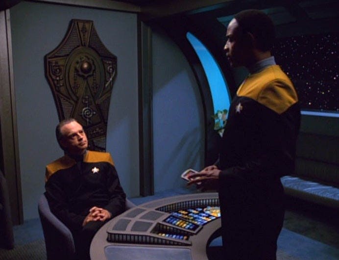 A sitting Suder is questioned by a standing Tuvok on Star Trek: Voyager