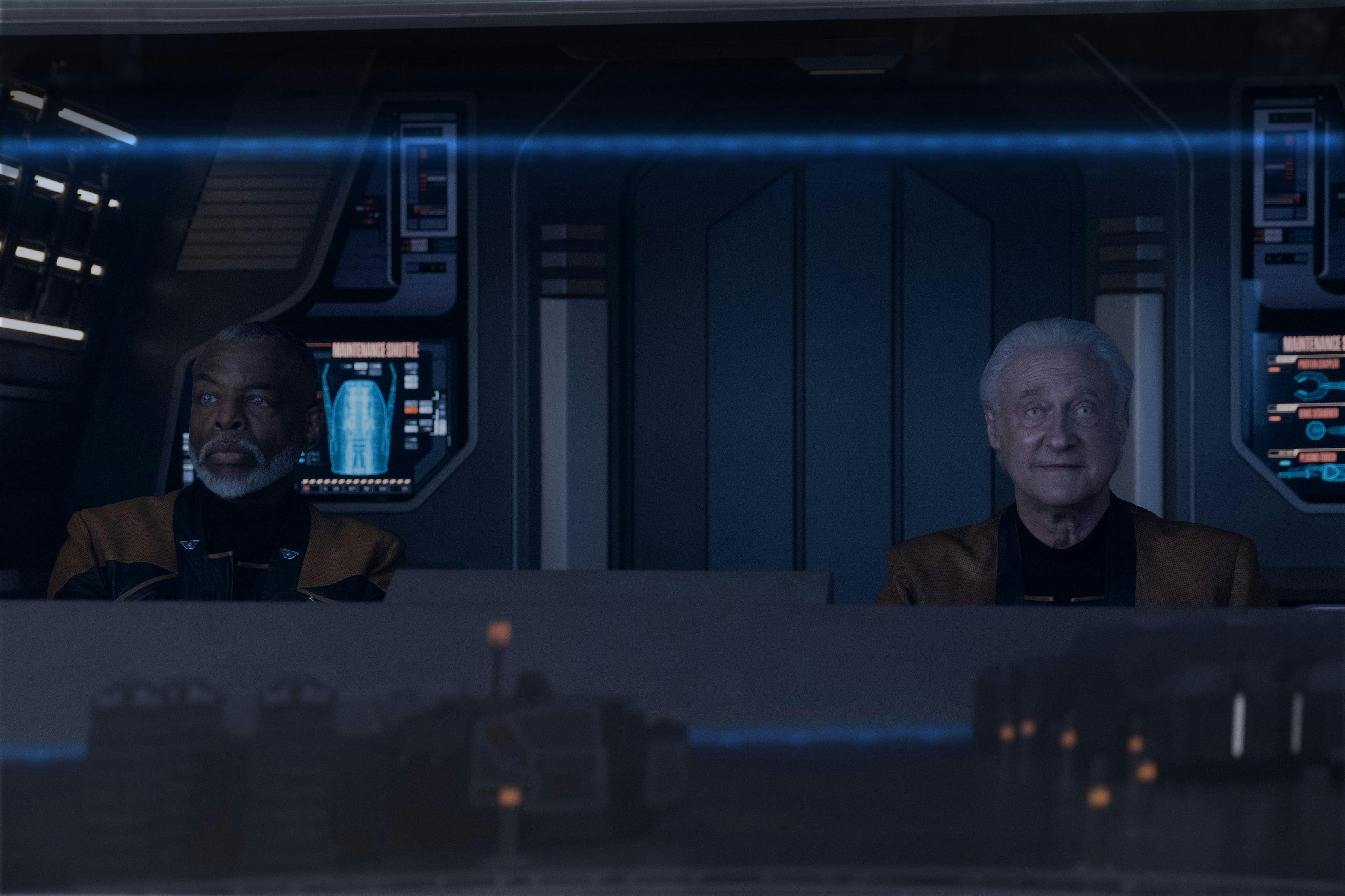 In a shuttle, Commodore Geordi La Forge looks off to his left with a blank expression as Data with a smile looks ahead of himself (Star Trek: Picard, "Vox")
