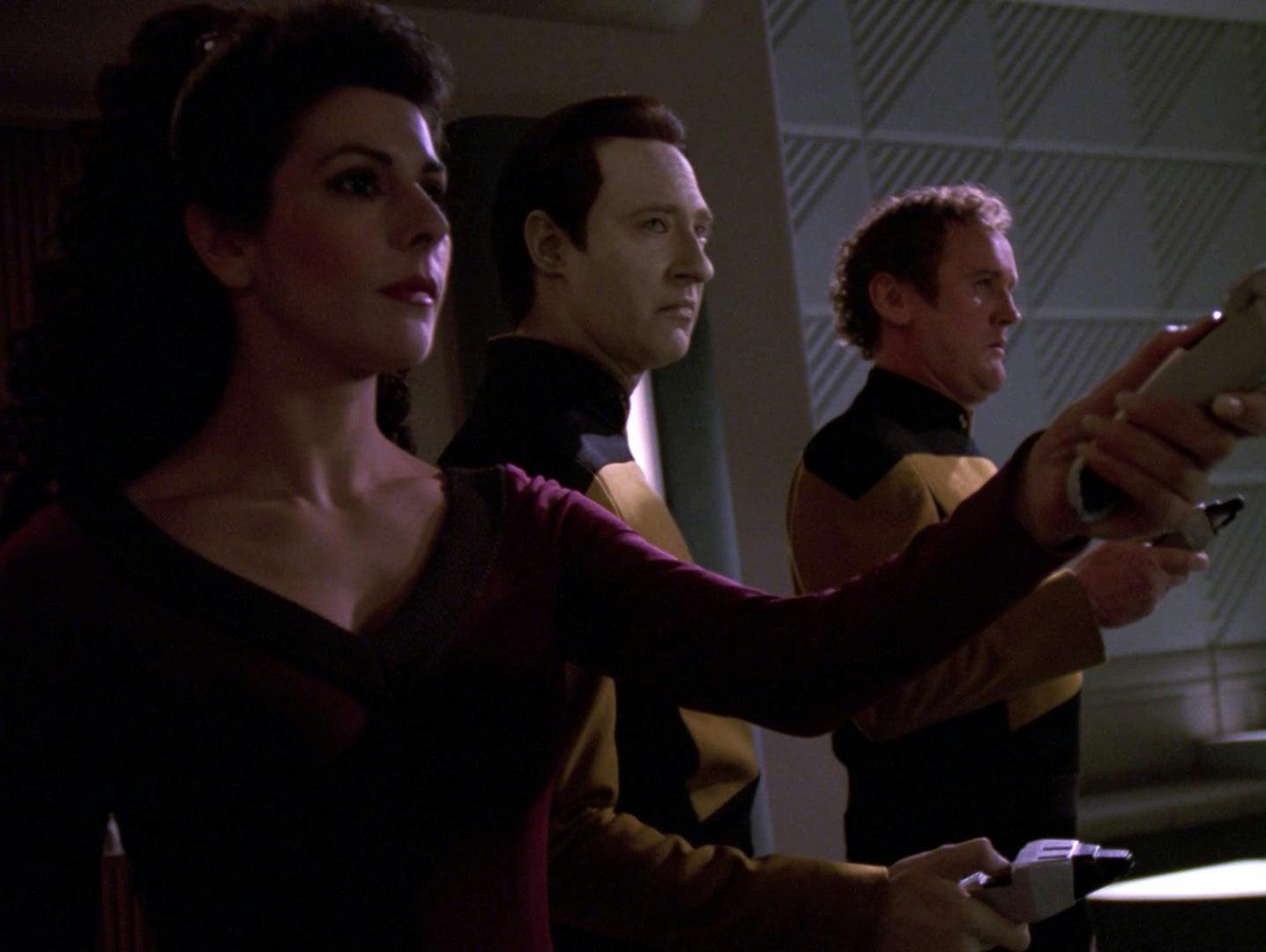 Troi, Data, and O'Brien, who have been possessed by aliens, hold the crew at phaser point.